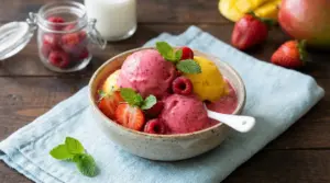 Coppa di gelato alla frutta con fragole, lamponi, mango e foglie di menta su tovagliolo azzurro