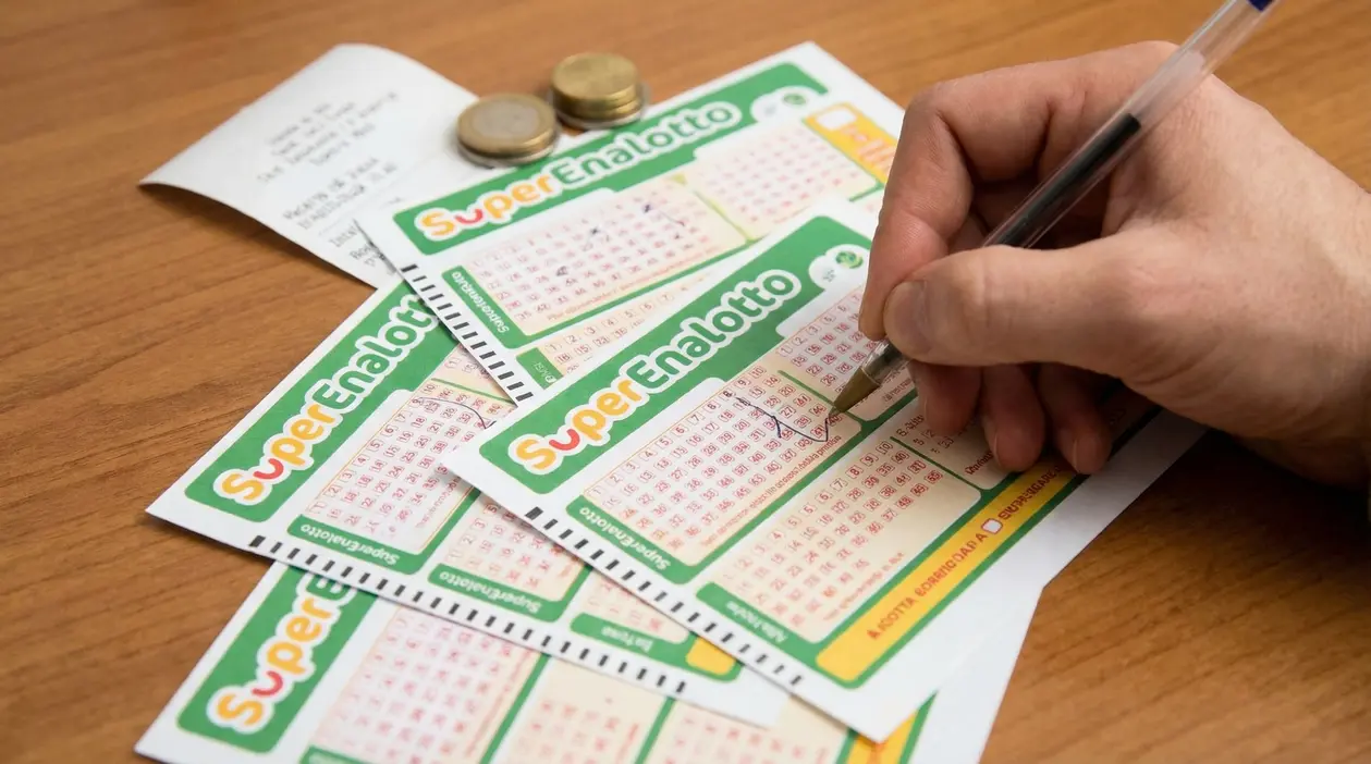 Una mano compila una schedina del SuperEnalotto su un tavolo di legno